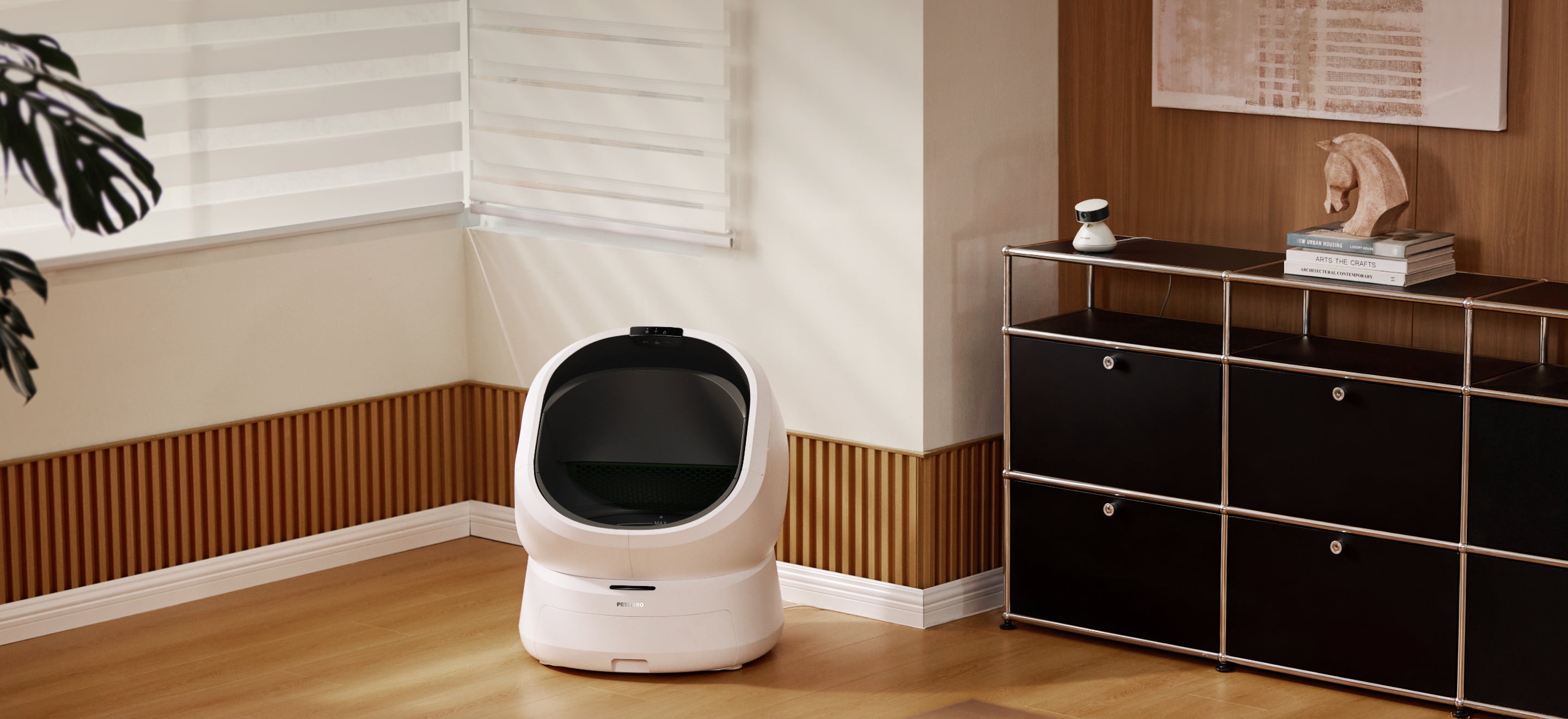 Petlibro automatic self-cleaning cat litter box in white, placed in a modern living room corner with wooden flooring and black storage cabinet nearby