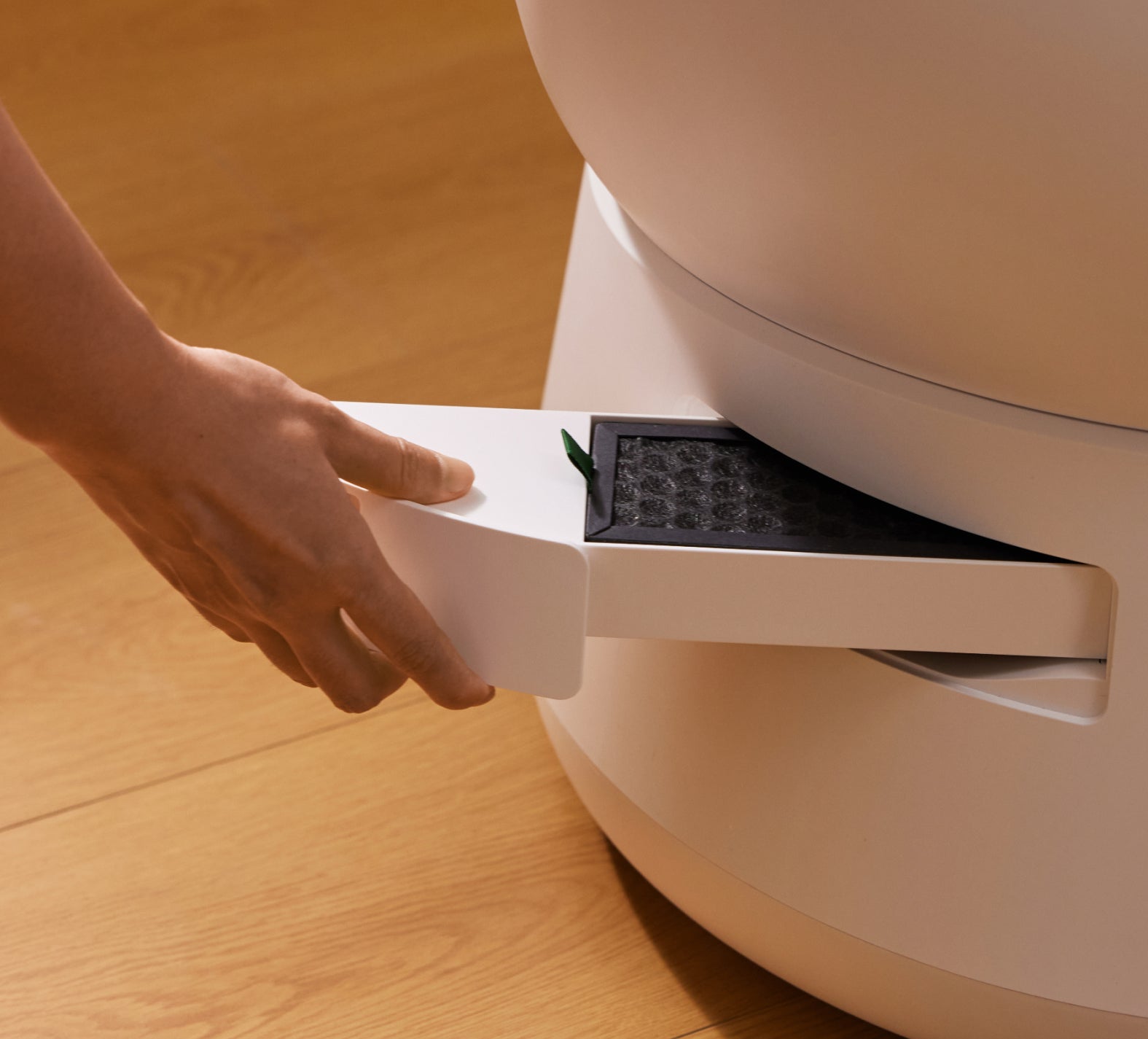 Petlibro white automatic cat litter box with a hand pulling out the black filter drawer on a wooden floor