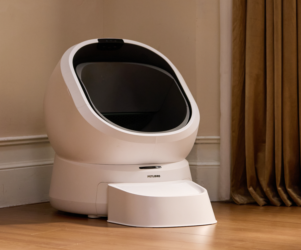 Petlibro PETLIBRO pet litter box, white automatic enclosed design with black opening and step, on wood floor by curtain