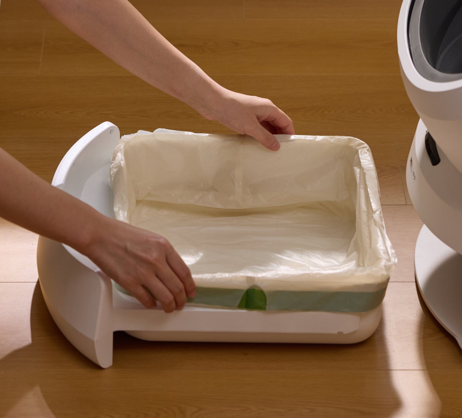 Petlibro white automatic cat litter box with removable tray and disposable liner being installed on wooden floor