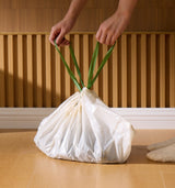 Petlibro white pet waste bag with green drawstring handles held by hands on wooden floor