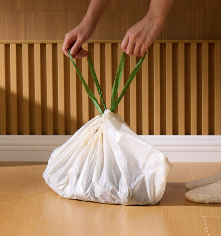 Petlibro white pet waste bag with green drawstring handles held by hands on wooden floor